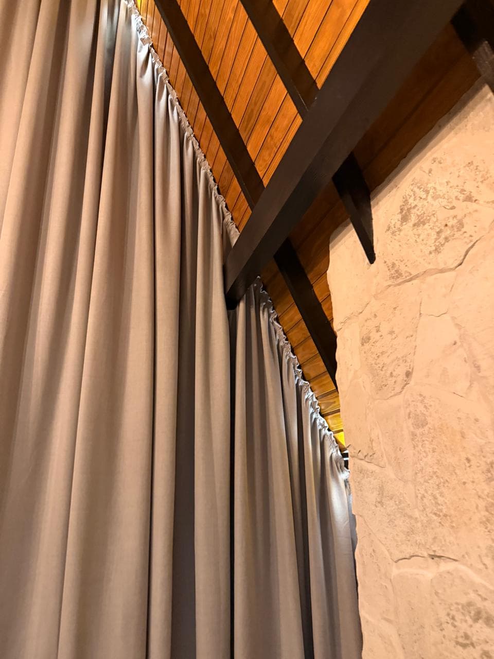 Detalhe das dobras e do trilho da cortina junto ao teto de madeira e à parede de pedra